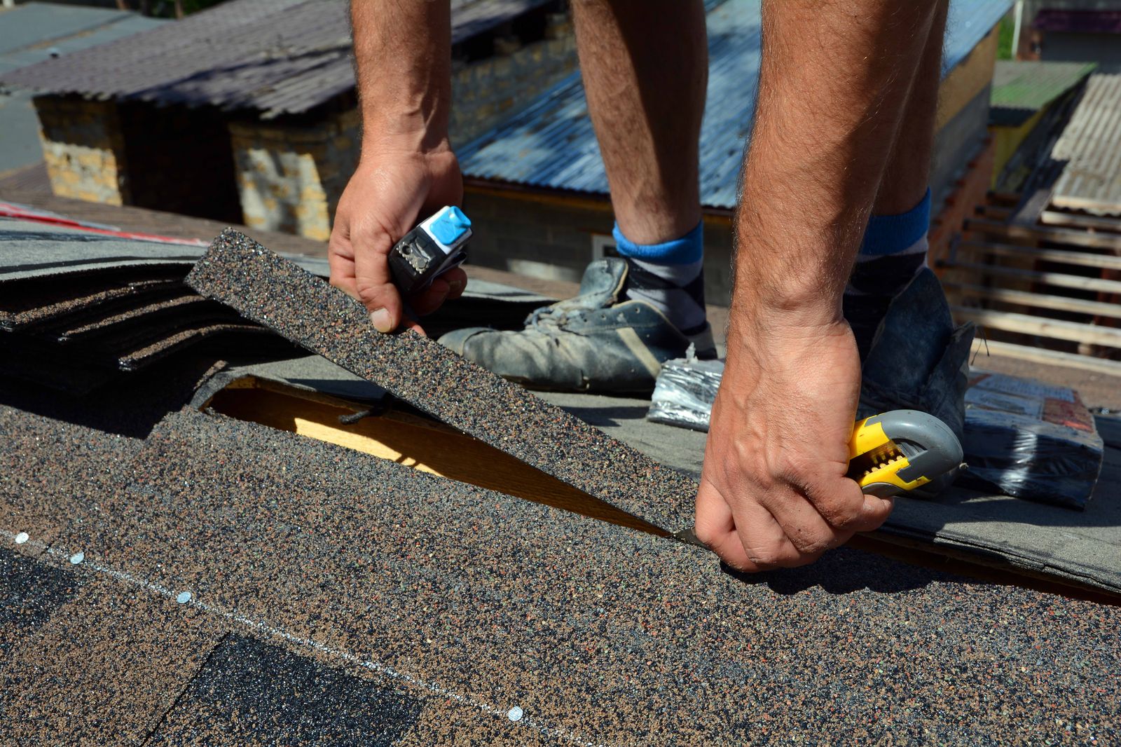 Placeholder. Roofer's hands trimming a shingle with a utility knife on a roof deck