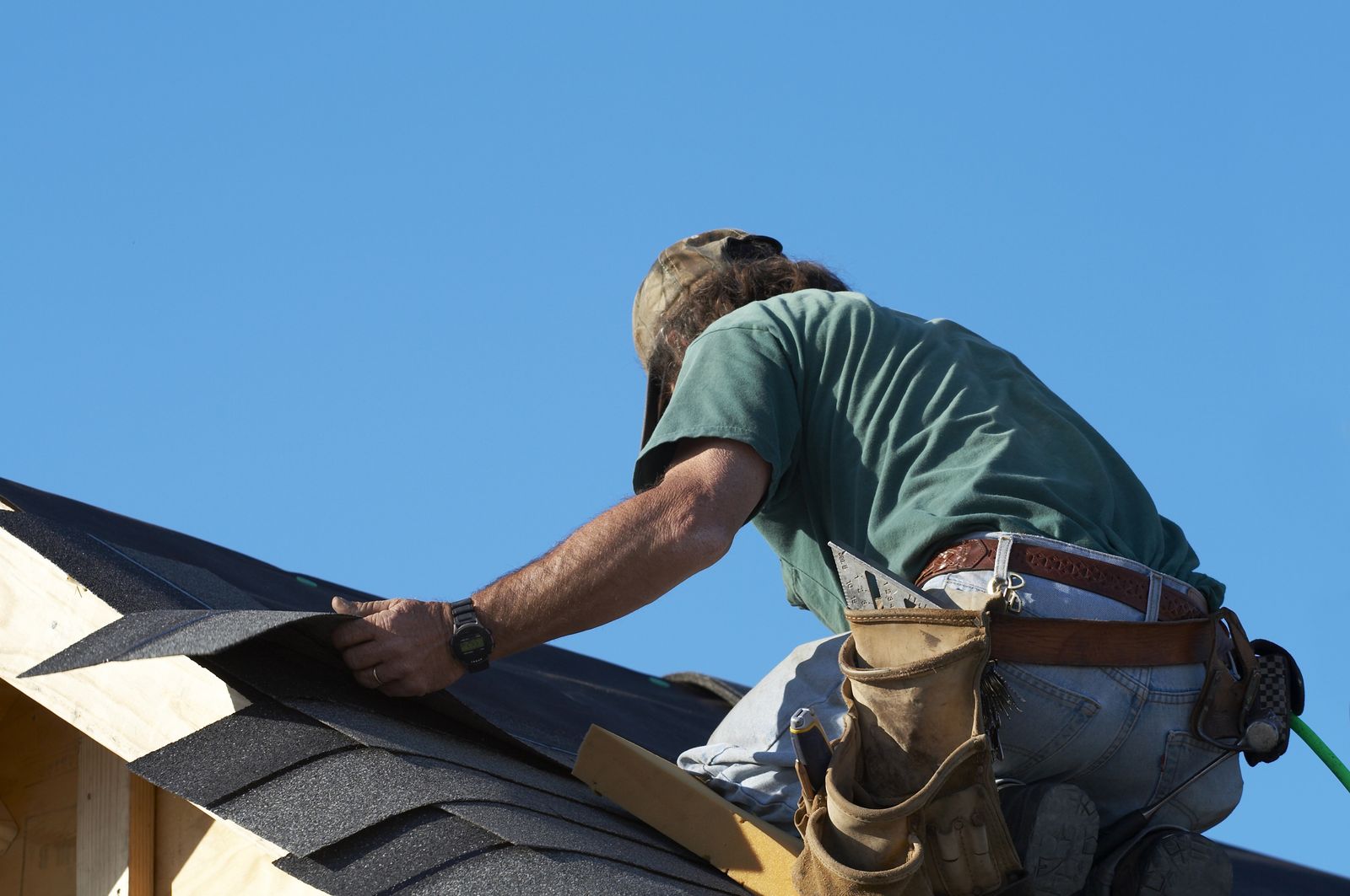 Placeholder. Roofer setting the first course of architectural shingles at the eave of a new roof deck