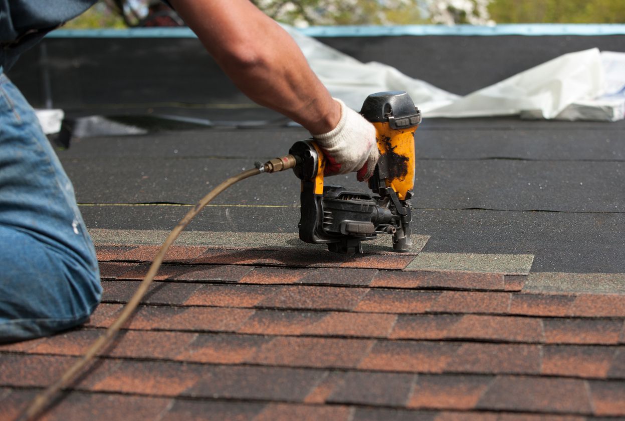 Placeholder. Roofer driving nails into a course of shingles with a pneumatic nail gun